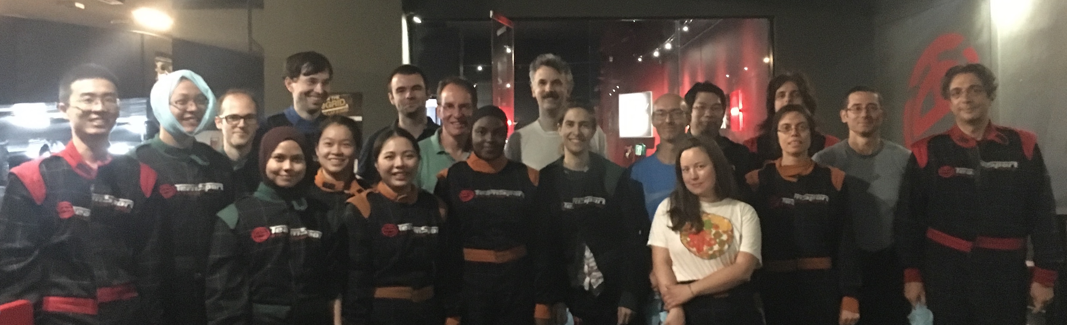 Two rows of people in karting attire and mostly with happy faces.