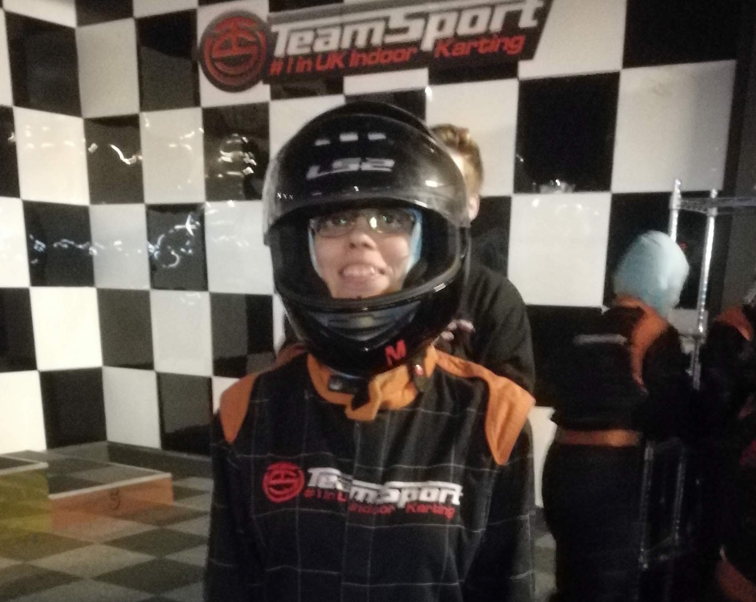 Three people in karting attire arm to arm standing in front of a sign that saus Team Sport #1 in UK Indoor Karting