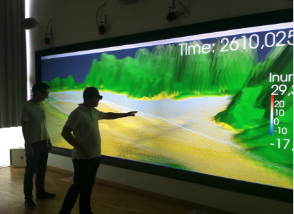Two men standing in front of a screen that is much larger than their bodies pointing to a map on the screen.