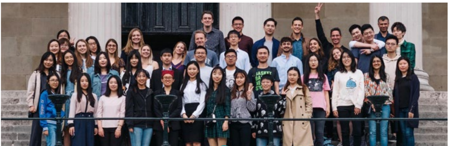 A bunch of people in the department posing in three rows on steps. There are three columns in the background.